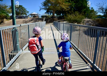 I bambini piccoli in sella a una moto e scooter attraverso un ponte pedonale, Aplin's weir a Ross River, Townsville, QLD, Australia Foto Stock