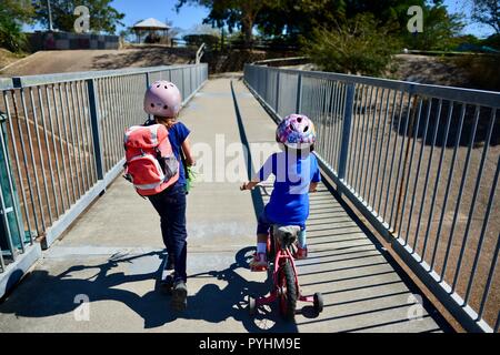 I bambini piccoli in sella a una moto e scooter attraverso un ponte pedonale, Aplin's weir a Ross River, Townsville, QLD, Australia Foto Stock