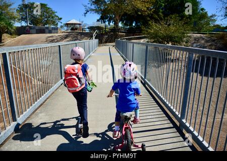 I bambini piccoli in sella a una moto e scooter attraverso un ponte pedonale, Aplin's weir a Ross River, Townsville, QLD, Australia Foto Stock