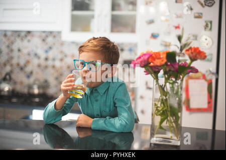 Funny carismatico stile retrò little boy in bicchieri di bere la limonata in cucina pensando Foto Stock