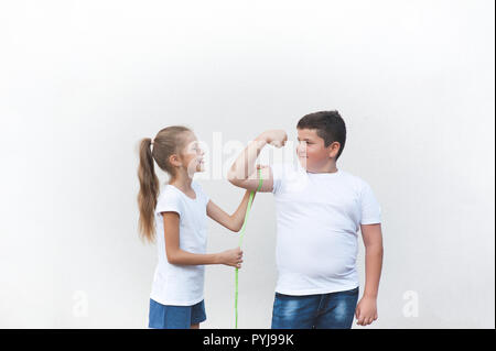 Un sano slim bambina tease Big fat boy misurando il suo muscolo con copyspace di nastro Foto Stock