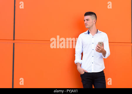 Giovane uomo bello tenendo il telefono cellulare e il pensiero Foto Stock