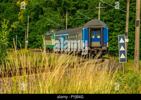 Un verde locomotiva elettrica passando la campagna ceca. Un treno che corre attraverso la valle verde. Il trasporto ferroviario in Repubblica Ceca. Una giornata di sole Foto Stock