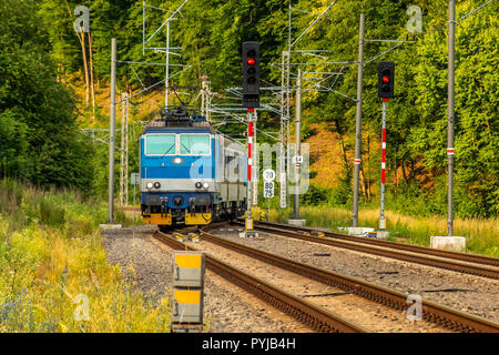 Un blu locomotiva elettrica passando la campagna ceca. Un treno che corre attraverso la valle verde. Il trasporto ferroviario in Repubblica Ceca. Una giornata di sole Foto Stock