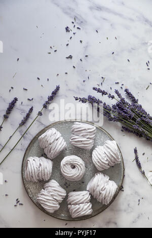 Laici piatta con una piastra di fatti in casa a base di marshmallows (zephyr, meringue) realizzato con lavanda su bianco marmor sfondo di pietra Foto Stock