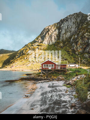 Tradizionale in rosso fishin casa in Bjoernsand vicino a Reine in Lofoten, Norvegia con red rorbu case. Pomeriggio al Tramonto con le nuvole su di una spiaggia di sabbia. Foto t Foto Stock