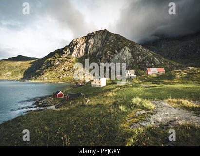 Tradizionale in rosso fishin casa in Bjoernsand vicino a Reine in Lofoten, Norvegia con red rorbu case. Pomeriggio al Tramonto con le nuvole su di una spiaggia di sabbia. Foto t Foto Stock