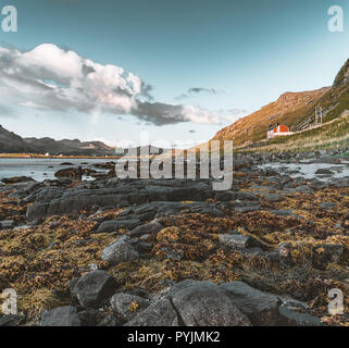 Tradizionale in rosso fishin casa in Bjoernsand vicino a Reine in Lofoten, Norvegia con red rorbu case. Pomeriggio al Tramonto con le nuvole su di una spiaggia di sabbia. Foto t Foto Stock