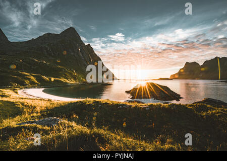 Tramonto con sunstar sulla spiaggia con le montagne sullo sfondo vicino Tangstad nelle Isole Lofoten in Norvegia. Una bellissima spiaggia di sabbia con vista montagne. Pho Foto Stock