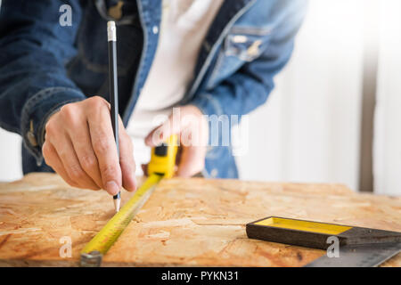 Carpenter operando con cautela guardando i piani di lavoro in falegnameria. Egli è imprenditore di successo al suo posto di lavoro. martellare un chiodo supporta sulla build Foto Stock
