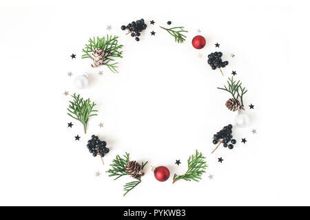 Cerchio di Natale composizione floreale. Ghirlanda di cipresso verde rami, coni di larice, Natale palle di vetro, baubles, argento coriandoli stelle e nero ligustro, bacche. Tavolo bianco sullo sfondo. Flatlay Foto Stock