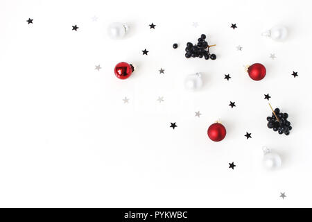 Composizione di natale. Rosso e Bianco Natale palle di vetro, baubles, argento coriandoli stelle e nero ligustro, Ligustrum bacche di colore bianco su sfondo tabella. Appartamento laico, vista dall'alto. Decorative pattern d'inverno. Foto Stock