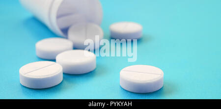 Diverse compresse bianche ricade al di fuori del vaso in plastica sulla superficie blu. Immagine di sfondo sul farmaceutico e medico, argomenti Foto Stock