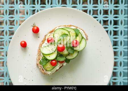 Un tocco mediterraneo su bruschette con crema di formaggio, menta, cetrioli e pomodori mini su uno sfondo grafico. Foto Stock