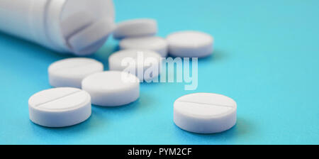 Diverse compresse bianche ricade al di fuori del vaso in plastica sulla superficie blu. Immagine di sfondo sul farmaceutico e medico, argomenti Foto Stock