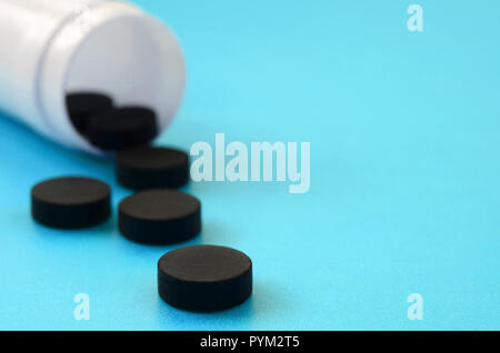 Diverse compresse nero ricade al di fuori del vaso in plastica sulla superficie blu. Immagine di sfondo sul farmaceutico e medico argomenti. Carbone attivo Foto Stock