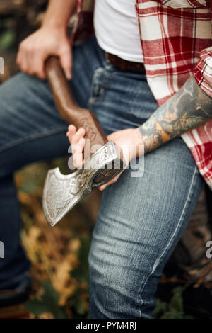 Chiudere l'Uomo in camicia a scacchi seduta su log e azienda ax Foto Stock