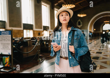 Viaggiatori femmina è in possesso di cellulare e trovare il giusto modo per andare. giovane turista texting tramite cellulare smartphone app nella stazione ferroviaria di ur Foto Stock