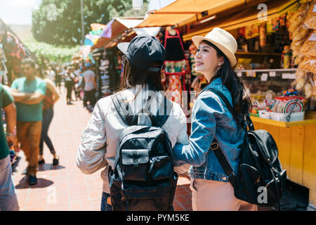 Vista posteriore di due femmina per i turisti che visitano il tradizionale mercato. bella signora guardando il fornitore che hanno camminato da. Il concetto di amicizia con y Foto Stock