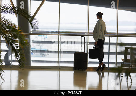 La donna come un passeggero che guarda fuori dalla finestra nell'area di attesa nel terminal dell'aeroporto Foto Stock