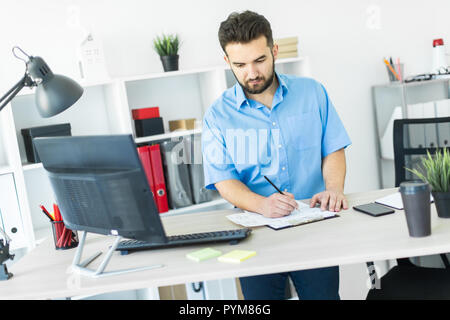 Un giovane uomo in piedi in ufficio e lavorare al computer a tavolo. Foto Stock