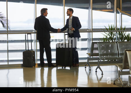 Due uomini d'affari in viaggio d'affari presso la stretta di mano in aeroporto area di attesa Foto Stock