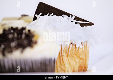 Piuttosto il cocco frosted cupcake decorate con un cuneo di cioccolato fondente. Estrema profondità di campo con il fuoco selettivo sul cupcake del centro. Foto Stock