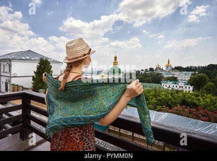 La donna nel cappello con sciarpa guardando alla chiesa con cupole dorate a Kiev Pechersk Lavra complesso cristiano. Vecchia architettura storica a Kiev, Ucraina Foto Stock
