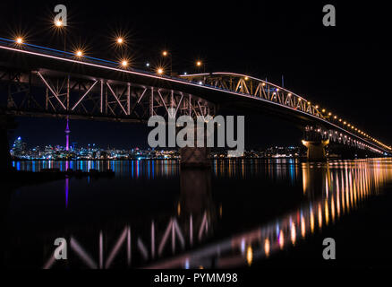 Auckland Harbour Bridge di notte comprese le luci del vettore, con Auckland Sky Tower (skytower) in background oltre il porto di Waitemata Foto Stock