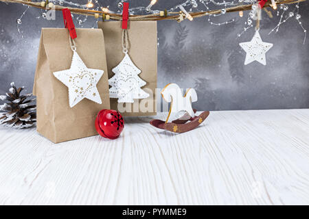 Natale fatti a mano sacchetti regalo, incandescente luce ghirlande e decorazioni appeso contro sfondo color argento Foto Stock