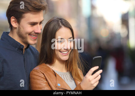 Felice coppia controllo smart phone contenuto in una vecchia città street Foto Stock