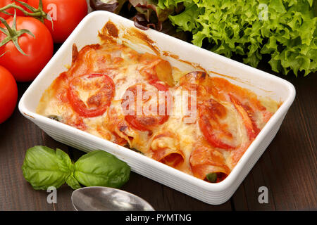 Caneloni ripiene di carne e formaggio fuso nella ciotola bianco su grunge Sfondo legno Foto Stock
