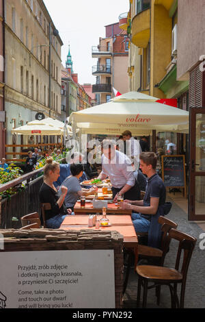 Wroclaw, vista in estate di un giovane turista giovane essendo servito il pranzo al fresco in un ristorante con terrazzo in una strada stretta a Wroclaw Old Town, Polonia. Foto Stock