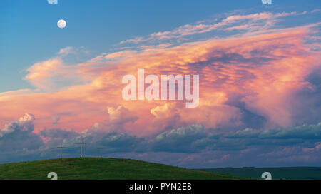 Nuvole drammatico riempie il cielo al tramonto. Primo piano verde collina con tre croci Foto Stock