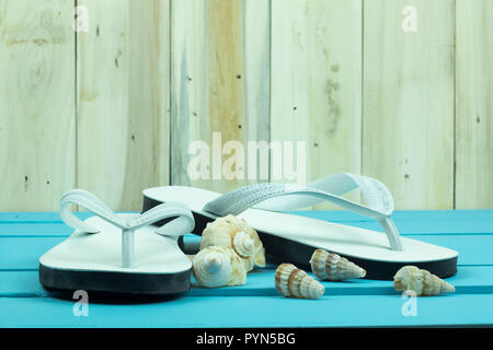 White flip flop con shellfishs sull'azzurro del tavolo di legno. Foto Stock