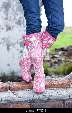 Stivali funky. Signora indossando gumboots colorati. In piedi su una parete di rovina. Foto Stock