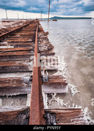 Rusty razy rotaie e traversine marcio coperto di sale sulla vecchia ferrovia tracce su una collinetta a miniere di sale vicino lago di salamoia. Foto Stock