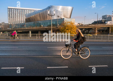 Due eco friendly donne ciclisti utilizzare un ciclo corsia sulla strada di Stoccolma, con Stoccolma Waterfront edificio in background, Stoccolma, Svezia. Foto Stock