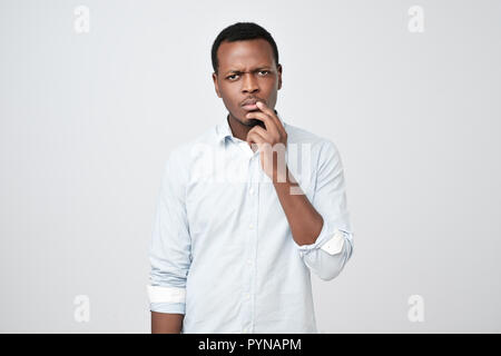 Malinconici grave perplesso uomo africano toccando il suo mento, guardando pensosa e scettico Foto Stock