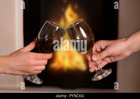 L uomo e la donna di tostatura a mano bicchieri di vino davanti al caminetto acceso a casa. Inverno romantico di notte per il giovane in amore. Close up, il fuoco selettivo Foto Stock