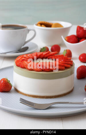 Demo di cottura. No-bake a due strati mini Strawberry Cheesecake matcha. Fette di fragola decorano la parte superiore della torta. 3 tazze di caffè, biscotti e s Foto Stock