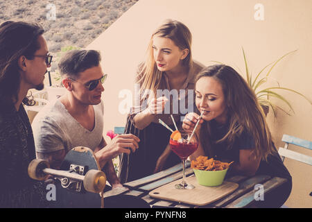 Gruppo con quattro persone due uomini due donne godere insieme in amicizia all'esterno le attività per il tempo libero a casa di bere da un bicchiere grande con vino rosso un Foto Stock