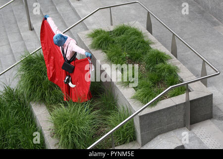Una ragazza in abito rosso i performa performance artistica in uno spazio pubblico. Molto elegante e brave le prestazioni nel centro della città di Milano. Foto Stock