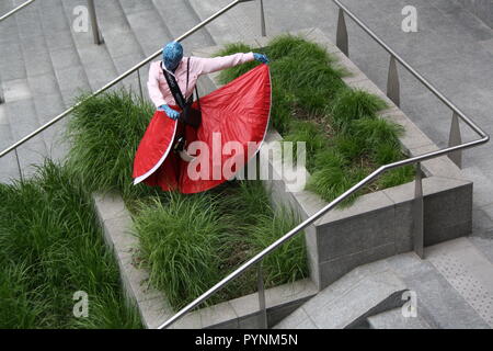 Una ragazza in abito rosso i performa performance artistica in uno spazio pubblico. Molto elegante e brave le prestazioni nel centro della città di Milano. Foto Stock