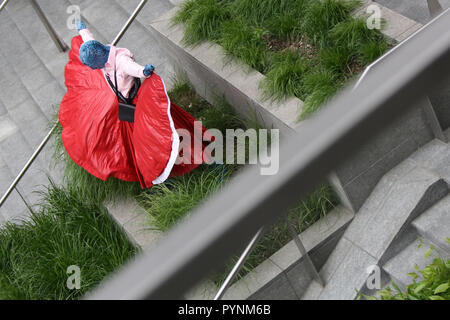 Una ragazza in abito rosso i performa performance artistica in uno spazio pubblico. Molto elegante e brave le prestazioni nel centro della città di Milano. Foto Stock