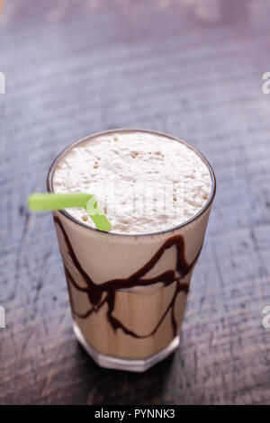 White Frappé Caffè di vetro con una bevanda ghiacciata con lo sciroppo al cioccolato al buio su un tavolo di legno in una caffetteria. Foto Stock