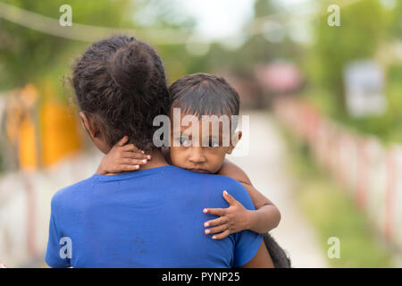 Villaggio TUNGU, isole Aru, Indonesia, dicembre 04, 2017 : una madre sta portando il suo bambino nella strada del villaggio di Tungu nell'ARU isola, ho Foto Stock