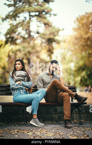 Coppia giovane è seduta in autunno il parco della città sul banco, quarreling. Sono arrabbiati e infelici e non guardando ogni altro. Foto Stock