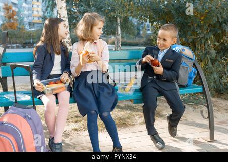 Outdoor ritratto di gli studenti della scuola elementare con pranzo scatole, scuola di sana prima colazione. I bambini mangiano, parlare, ridere. Foto Stock