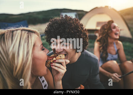 Felice coppia giovane godetevi una bella giornata in natura. Essi sono la grigliatura salsicce, mangiare, ridendo e parlando felici di essere insieme. Foto Stock